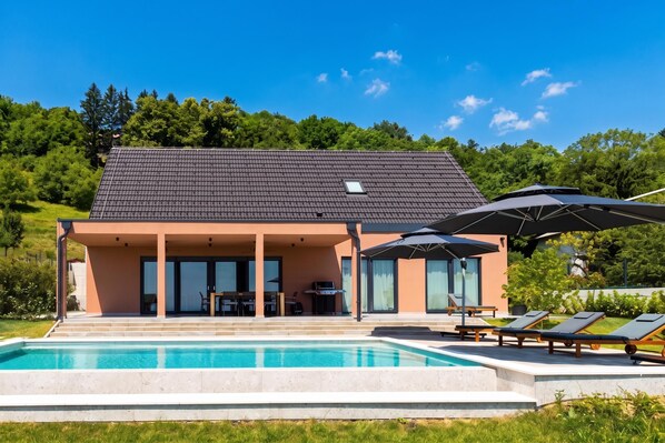 A modern house with a swimming pool, outdoor seating, and a covered patio.