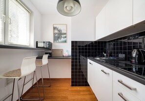 A compact kitchen with a black countertop, white cabinets, and a wooden floor. - Rondo ONZ Homely Apartment (Warszawa)
