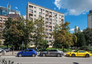 A multi-story residential building with balconies, a street with cars, and trees. - Rondo ONZ Homely Apartment (Warszawa)
