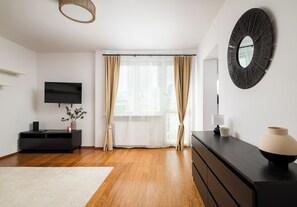 A modern living room with a flat-screen TV, a dark wooden dresser, a round mirror, and a large window with sheer curtains. - Rondo ONZ Homely Apartment (Warszawa)