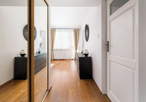 A hallway with a wooden floor, a mirror, and two black side tables with lamps. - Rondo ONZ Homely Apartment (Warszawa)