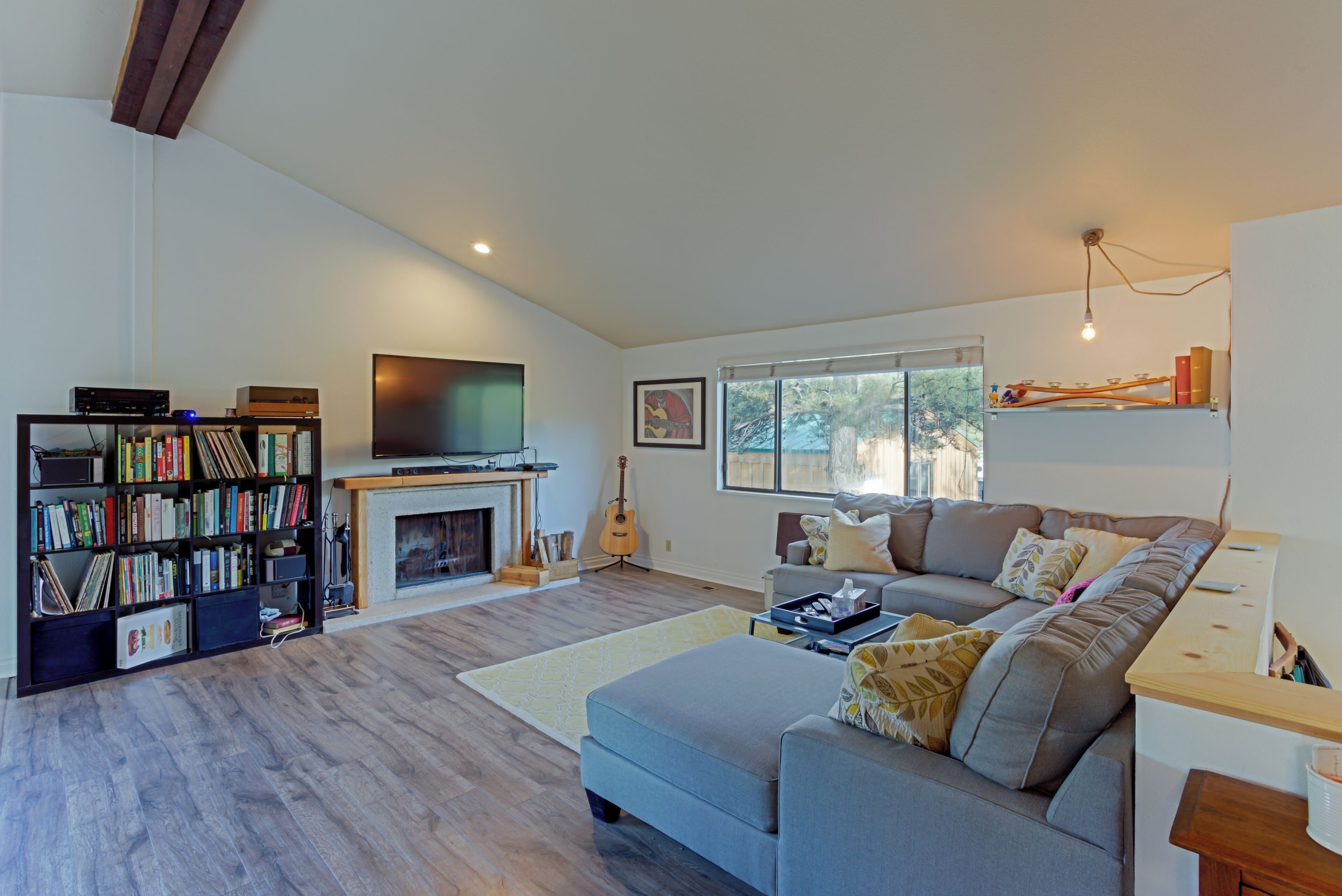 A living room with a fireplace, a television, a bookshelf, a sofa, and a window with a view of trees.