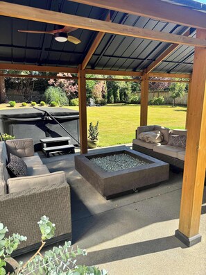 Eine Terrasse im Freien mit überdachter Sitzgruppe, einem Feuerkorb und Blick auf eine gepflegte Rasenfläche.