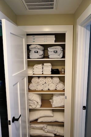 A walk-in closet with shelves containing folded towels, rolled towels, and storage bins.