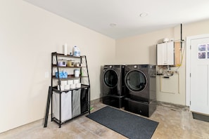 A laundry room with two black front-loading washers, a metal drying rack, and a white utility room with a water heater.
