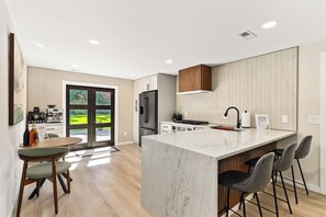 A modern kitchen with a large island, bar stools, and a dining area with a view.