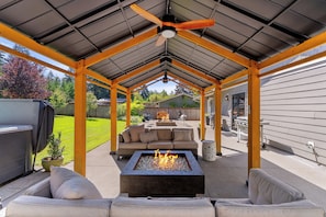 A covered outdoor patio with a fire pit, seating area, and a ceiling fan.