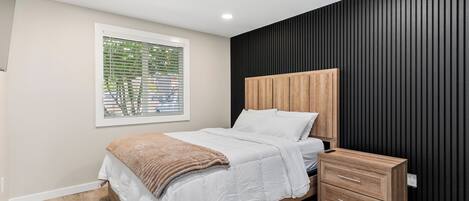 A modern bedroom with a wooden bed, a bedside table, and a window with blinds.