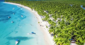 A beach with clear turquoise waters, boats, and a line of palm trees.