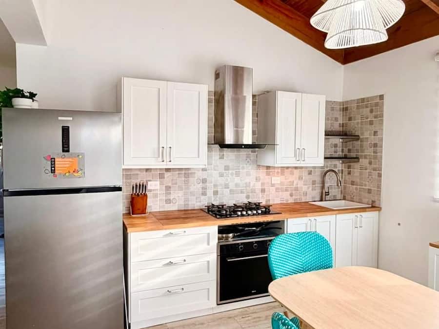 Una cocina moderna con armarios blancos, un refrigerador de acero inoxidable, una estufa a gas y una mesa de comedor de madera con dos sillas.