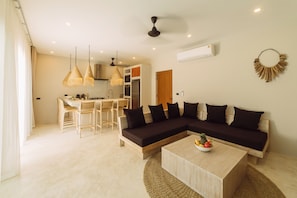 A modern living room with a sectional sofa, a dining area with a table and chairs, and a kitchen in the background.