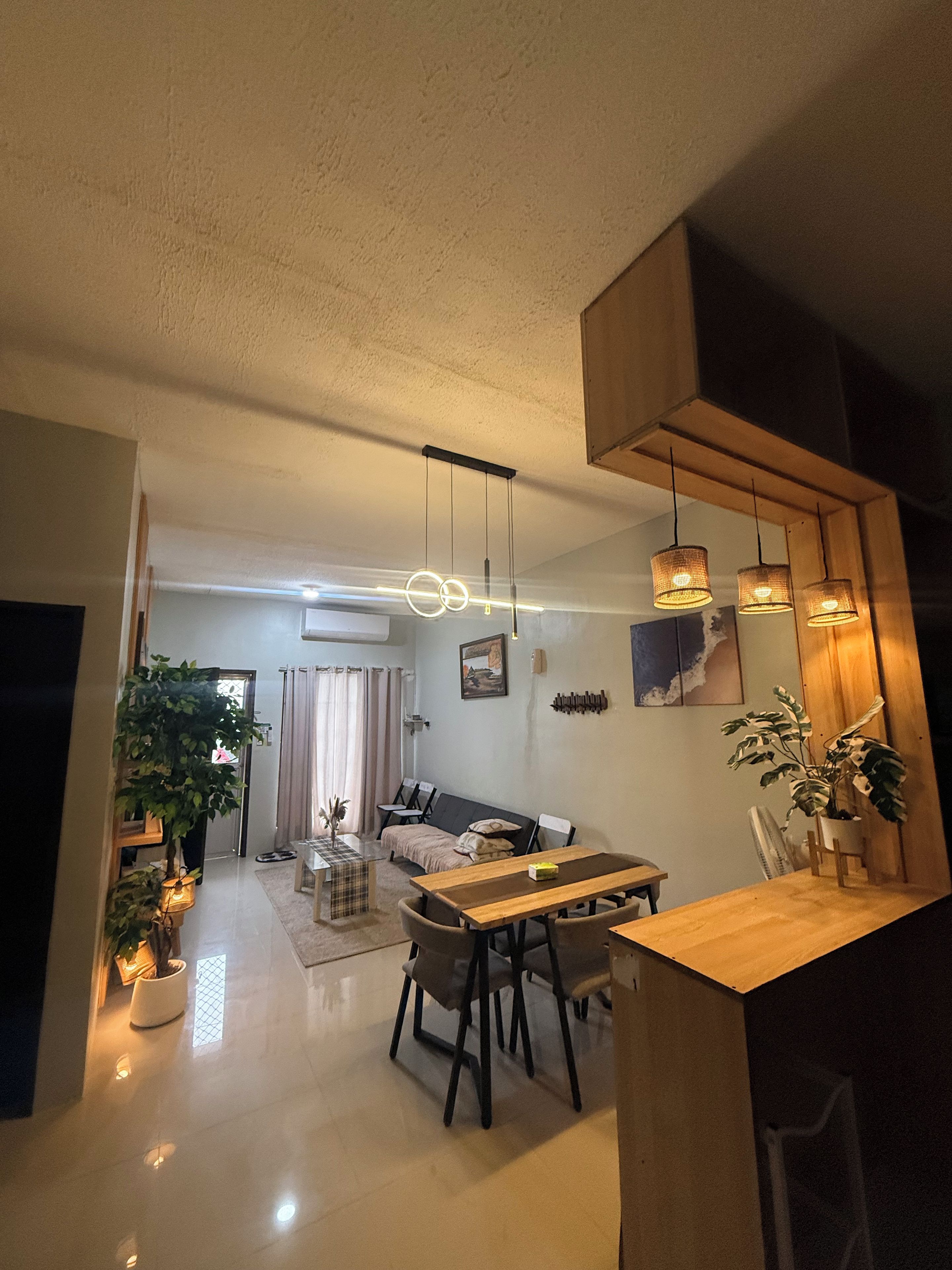 Una sala de estar moderna con comedor, que incluye un sofá, una mesa de comedor de madera y lámparas colgantes.