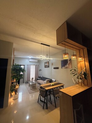 A modern living room with a dining area, featuring a sofa, a wooden dining table, and hanging pendant lights.