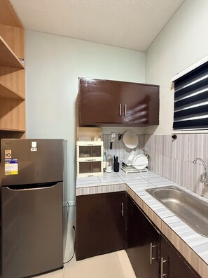 A compact kitchen with a built-in refrigerator, a sink, and a cabinet above the countertop. - Kamayo Guest House l 2BR Spacious •Near Dahican beach (City of Mati)