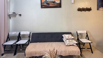 Ein Zimmer mit einem Bett, zwei Stühlen, einem Gemälde und einem kleinen Tisch mit einer Vase.