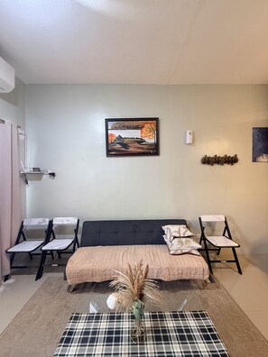 Una habitación con una cama, dos sillas, un cuadro y una mesita con un florero.