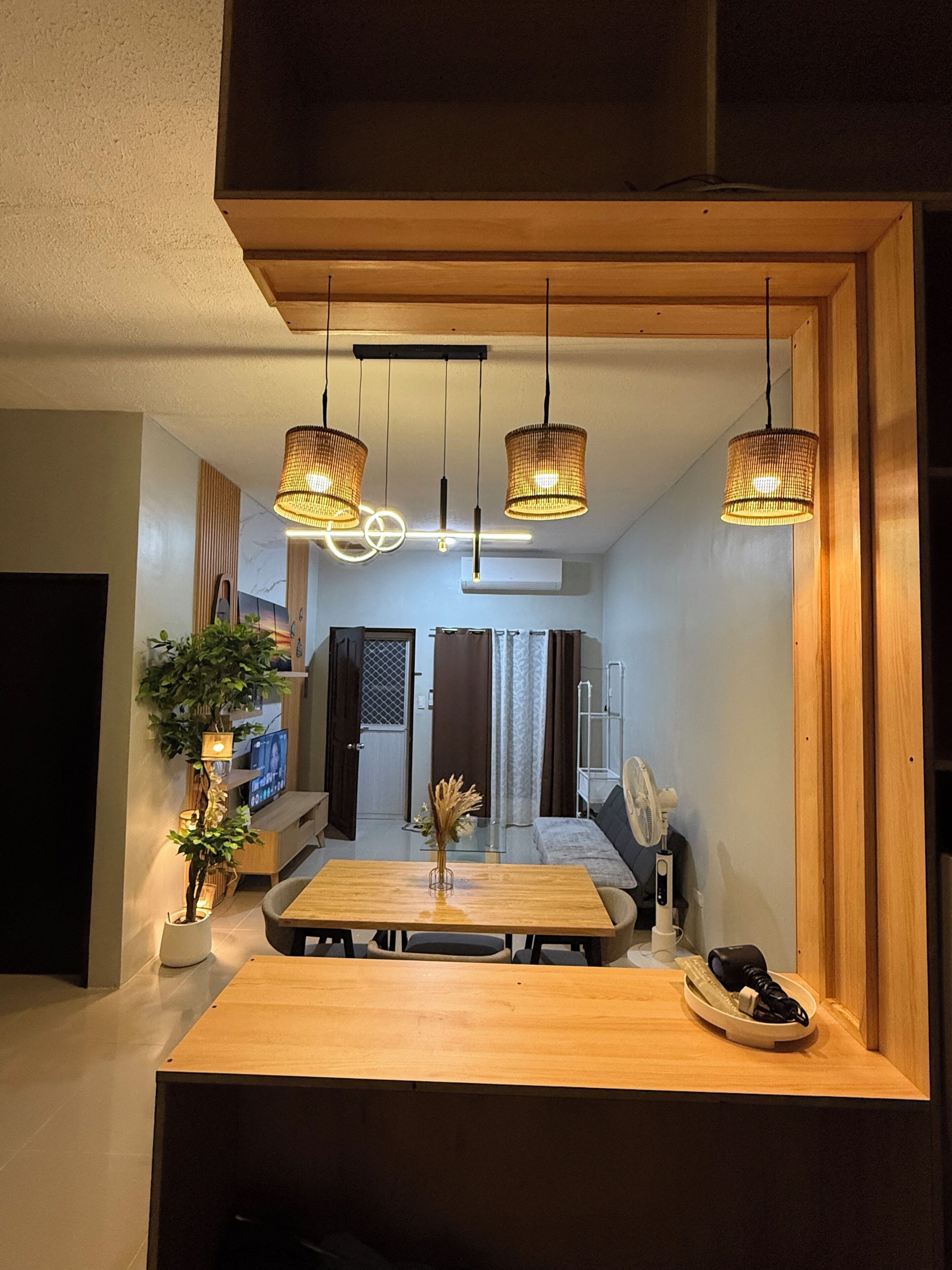 Een moderne eetruimte met een houten tafel, hangende rieten lampen en een potplant.