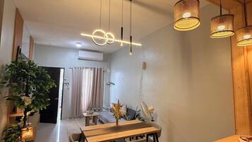 A modern dining area with a wooden table and chairs, pendant lights, and a potted plant.