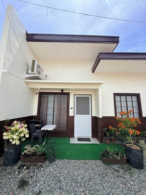 A residential building with a front door, a small porch area with a table and chairs, and a variety of potted plants.