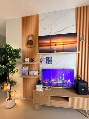 A modern living space with a wooden TV stand, a flat-screen TV displaying a cityscape, a potted plant, and a wall-mounted clock.