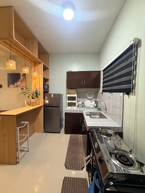 A compact kitchen with a refrigerator, stove, sink, and wooden cabinets.