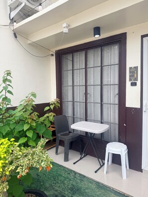 Un balcón con una mesa y sillas, una planta en maceta y una ventana con vidrio esmerilado.