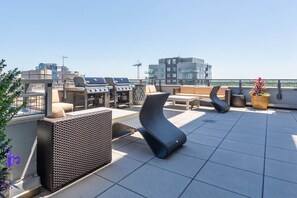 Eine Dachterrasse mit Außenmöbeln, Grillplatz und Blick auf die Stadtlandschaft.
