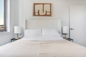A bedroom with a large bed, two bedside tables with lamps, a door, and a wall-mounted artwork. - Blueground | Woodmont Triangle, rooftop pool, nr Cabin John Regional Park (Bethesda)