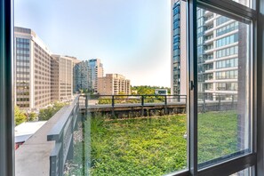A view from a window overlooking a green space with a bridge, modern buildings, and a clear sky. - Blueground | Woodmont Triangle, rooftop pool, nr Cabin John Regional Park (Bethesda)