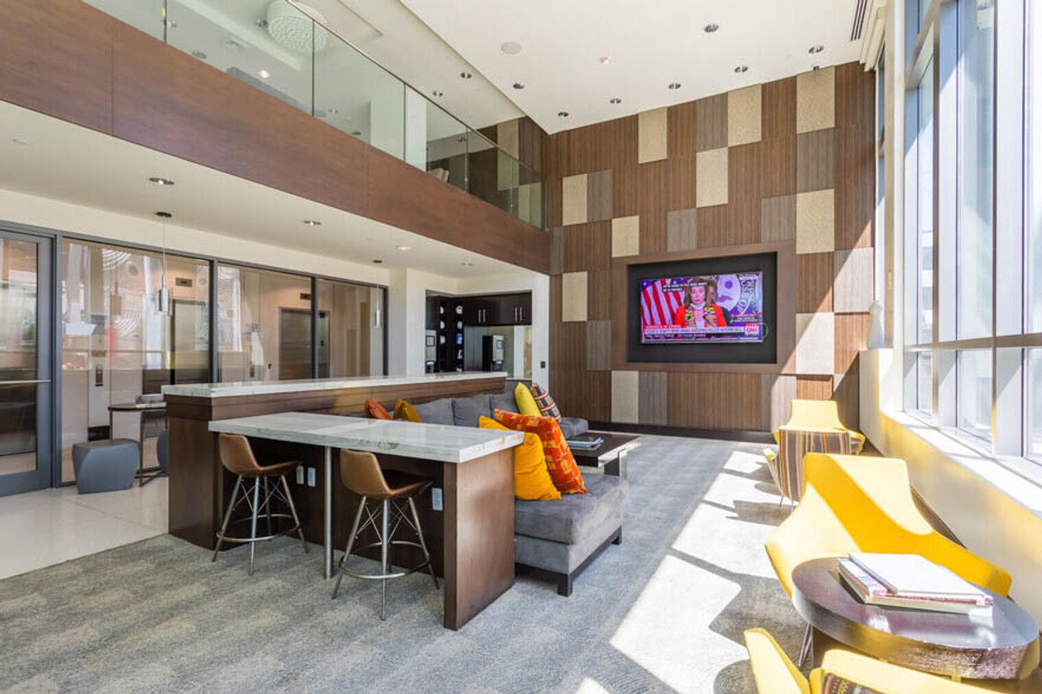 Una cocina moderna con una isla central, un comedor con taburetes de bar, una sala de estar con sofá y cojines coloridos, y un televisor montado en la pared.