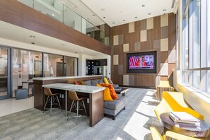 Eine moderne Küche mit Kochinsel, ein Essbereich mit Barhocker, ein Wohnzimmer mit Sofa und bunten Kissen sowie ein an der Wand befestigter Fernseher.