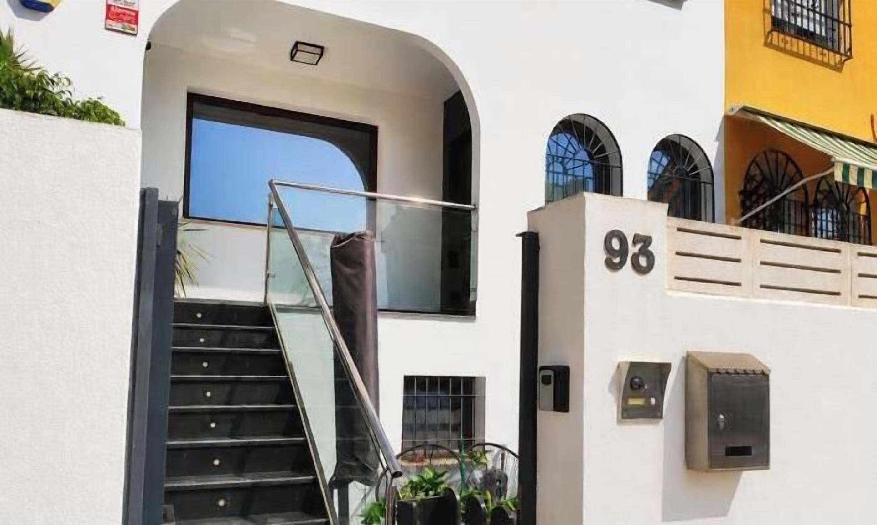 Una escalera con barandas de vidrio que conduce a una puerta, un buzón y el número 93.