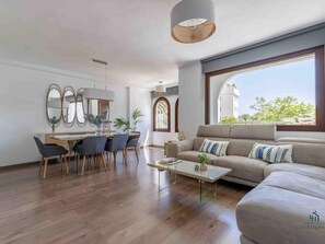 A modern living room with a sofa, coffee table, and dining area with chairs and a table. - Colina Hill Living4malaga (Torremolinos)