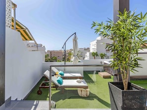 Eine Dachterrasse mit zwei Liegestühlen, einem kleinen Tisch und einem Blumentopf.