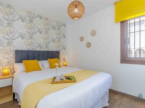 Quarto com cama, mesas de cabeceira, um criado-mudo, janela e parede decorada.