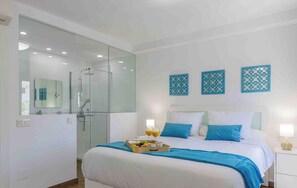 A modern bedroom with a glass-enclosed shower, a bed with blue bedding, and decorative wall art. - Colina Hill Living4malaga (Torremolinos)