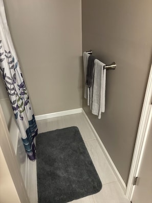 A bathroom with a shower curtain, a towel rack with two towels, and a dark rug on the floor.