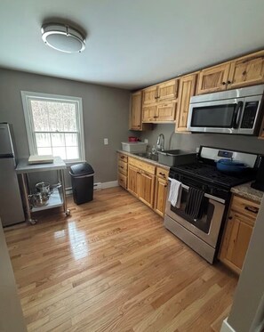 A kitchen with wooden cabinets, a stainless steel stove, a microwave, and a window with blinds. - Spacious Family Friendly 3-bedroom home in a woodsy area of Ashland, NH (Ashland)