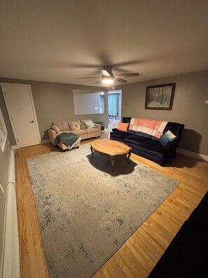 A living room with a ceiling fan, a wooden coffee table, a beige sofa, and a black sofa with a blanket.