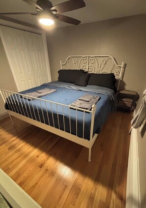 A bedroom with a metal bed frame, a white ceiling fan, a wooden floor, and a white door in the background.