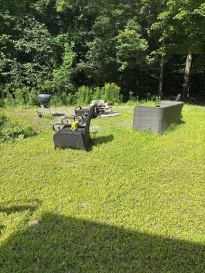 A grassy outdoor area with a grill, a stack of bricks, and a wicker chair. - Spacious Family Friendly 3-bedroom home in a woodsy area of Ashland, NH (Ashland)