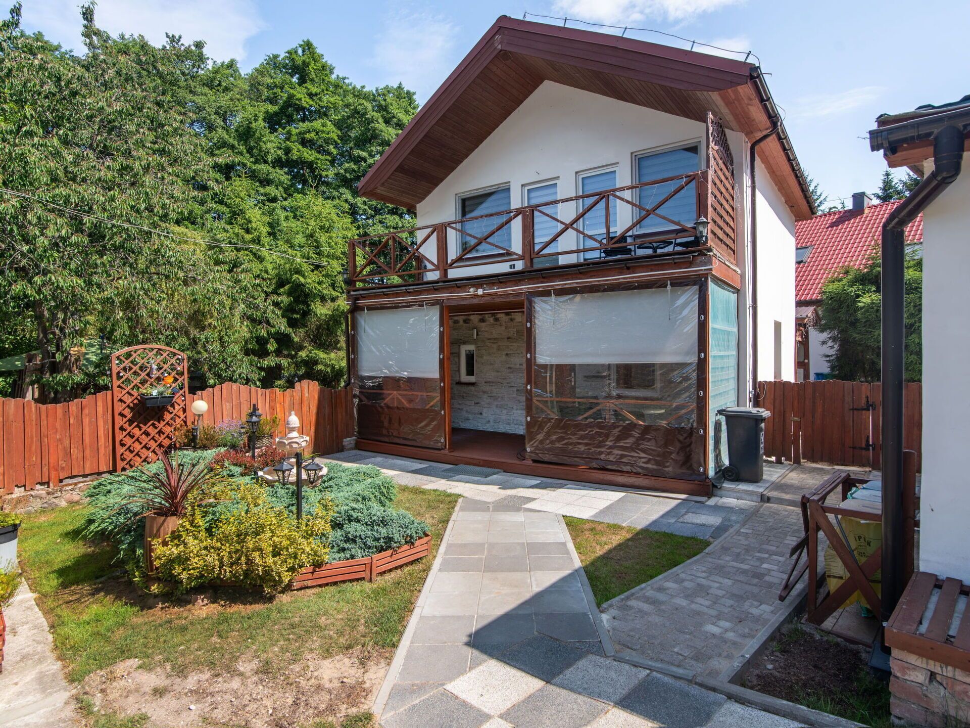 A two-story house with a balcony, a fenced garden, and a paved walkway.