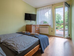 Ein Schlafzimmer mit Bett, Fernseher, Schminktisch und einem Fenster mit Vorhängen, mit Blick ins Freie.