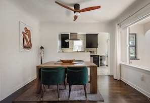A dining area with a wooden table, two green chairs, a ceiling fan, and a kitchen in the background. - The Ultimate LA 3BR Retreat Outdoor Lounge & BBQ (Los Angeles)