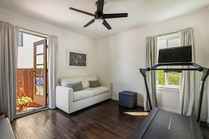 A room with a treadmill, a sofa, a ceiling fan, a window with curtains, and a door leading to an outdoor area. - The Ultimate LA 3BR Retreat Outdoor Lounge & BBQ (Los Angeles)