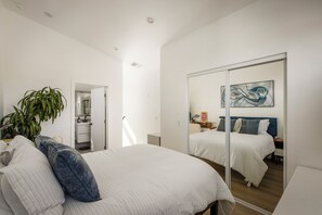 Ein Schlafzimmer mit einem Bett, einem Spiegel, einer Pflanze und einem Gemälde.