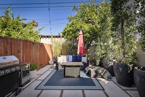 Eine Terrasse mit Grill, Gartenmöbeln und Kübelpflanzen.