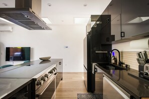 A modern kitchen with a stainless steel range, black cabinets, and a flat-screen TV. - The Ultimate LA 3BR Retreat Outdoor Lounge & BBQ (Los Angeles)