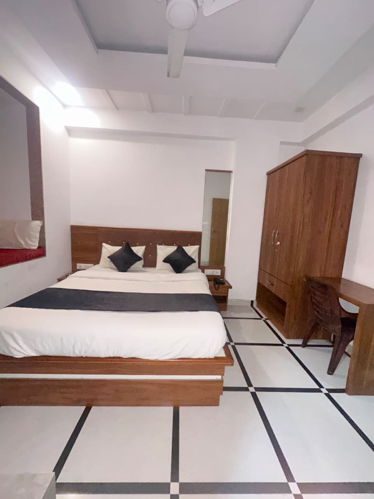 A bedroom with a bed, a wooden wardrobe, a desk, and a mirror.
