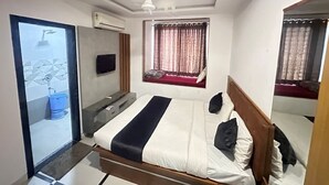 Un dormitorio con cama, televisor, ventana con cortinas, ventilador de techo y baño con ducha.